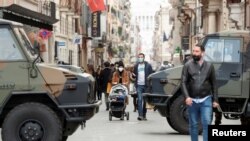 People walk past army vehicles at a street on the final day of open restaurants and bars before tighter coronavirus disease (COVID-19) restrictions are enforced, in Rome, Italy, March 14, 2021. 