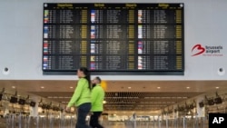 Dua pekerja bandara berjalan melewati tanda keberangkatan yang penuh dengan pembatalan selama aksi mogok nasional terhadap pemotongan anggaran federal di Brussels, Kamis, 13 Februari 2025. (Marius Burgelman/AP)