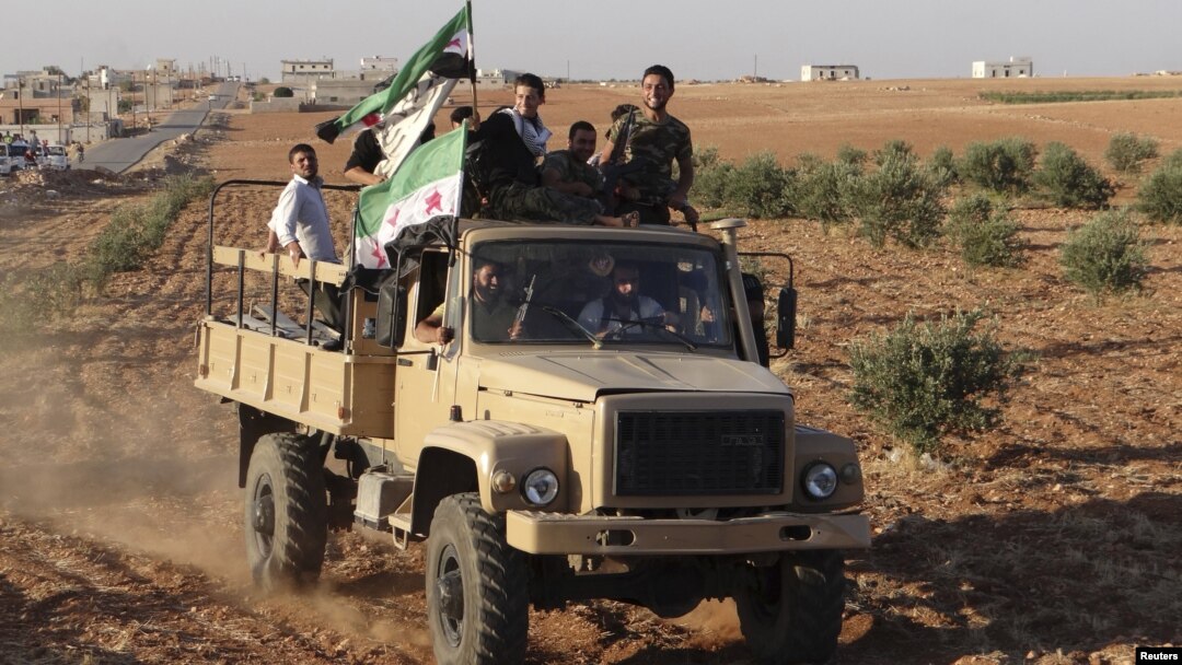 Các chiến binh thuộc Quân đội Syria Tự do cầm cờ của phe đối lập đi trên chiếc xe vận tải mà họ nói đã chiếm được từ lực lượng của chính phủ