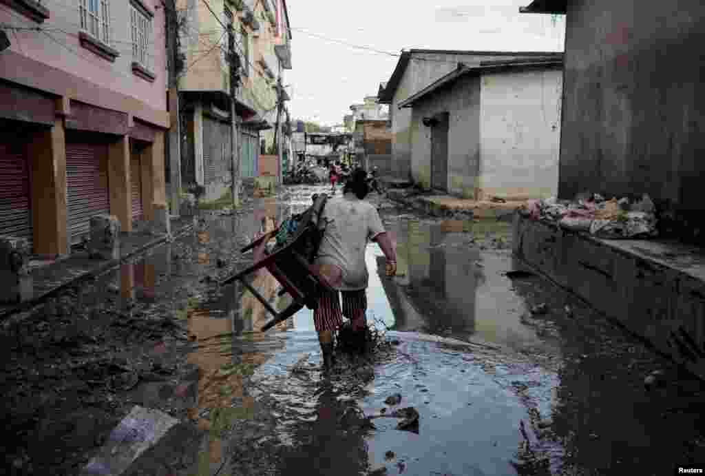 A woman carrying a chair walks along a muddy street as the floodwater recedes from a residential area that was flooded by the overflowing Bagmati River following heavy rains in Kathmandu, Nepal.