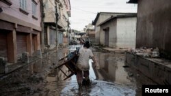 A woman carrying a chair walks along a muddy street as the floodwater recedes from a residential area that was flooded by the overflowing Bagmati River following heavy rains in Kathmandu, Nepal.