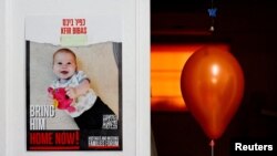 FILE - A balloon is placed next to a placard showing Kfir Bibas, as families call for his release, during a media tour, in Kibbutz Nir Oz, southern Israel, January 16, 2024.