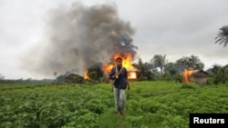 FILE - An ethnic Rakhine man holds homemade weapons as he walks in front of houses that were burnt during fighting between Buddhist Rakhine and Muslim Rohingya communities in Sittwe, June 10, 2012. Myanmar's outgoing government lifted a nearly four-year curfew in the western state of Rakhine on March 29, 2016, after communal violence.