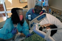 Patty Trejo, left, looks at her intubated husband, Joseph, in a COVID-19 unit as registered nurse Celina Mande holds a smartphone showing a mariachi band performing for the patient at St. Jude Medical Center, in Fullerton, California, Feb. 15, 2021.