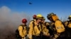 Firefighters of the Los Angeles County Fire Department gather while an helicopter flies, as the Palisades Fire rages on at the Mandeville Canyon, in Los Angeles, California, Jan. 11, 2025. 