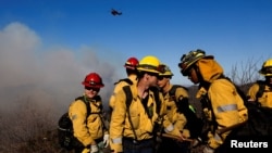 Firefighters of the Los Angeles County Fire Department gather while an helicopter flies, as the Palisades Fire rages on at the Mandeville Canyon, in Los Angeles, California, Jan. 11, 2025. 