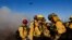 Firefighters of the Los Angeles County Fire Department gather while an helicopter flies, as the Palisades Fire rages on at the Mandeville Canyon, in Los Angeles, California, Jan. 11, 2025. 