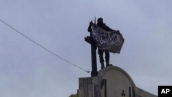 In this image posted on the Twitter page of Syria's al-Qaida-linked Nusra Front on Saturday, March 28, 2015, which is consistent with AP reporting, a fighter from Syria's al-Qaida-linked Nusra Front holds his group flag in Idlib province, north Syria.