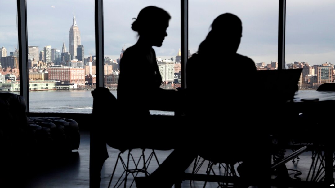 FILE - The New York City skyline is seen at a distance as two women are seen on their laptops in a building in Hoboken, New Jersey, Jan. 23, 2018. With privacy breaches on the rise, there is a growing push for greater online protection of consumers.