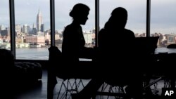 FILE - The New York City skyline is seen at a distance as two women are seen on their laptops in a building in Hoboken, New Jersey, Jan. 23, 2018. With privacy breaches on the rise, there is a growing push for greater online protection of consumers.