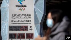 A woman wearing a face mask to protect against COVID-19 walks past a clock counting down the time until the opening ceremony of the 2022 Winter Olympics in Beijing, Jan. 15, 2022. 