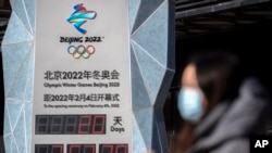 2022年1月15日，2022年北京冬季奧運會開幕前，一名戴著口罩的婦女走過倒計時鐘（美聯社）。