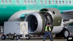 A worker walks past an engine on a Boeing 737 MAX 8 airplane being built for American Airlines at Boeing Co.'s Renton assembly plant, March 13, 2019, in Renton, Wash.