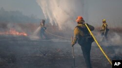 Firefighters work to prevent flames from reaching nearby homes as a helicopter drops water during the Easy Fire, Oct. 30, 2019, in Simi Valley, Calif.