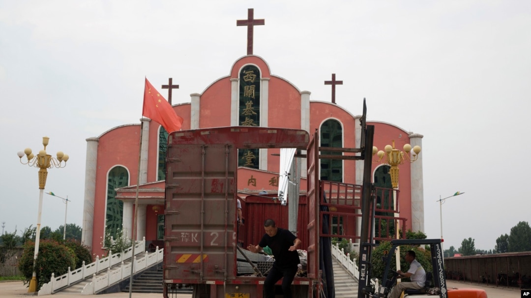 Seorang pekerja melompat dari sebuah truk yang diparkir di depan sebuah gereja dan bendera nasional Cina di dekat kota Pingdingshan di provinsi Henan China tengah, 2 Juni 2018. (Foto: dok).
