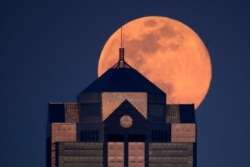 FILE - The supermoon rises behind a downtown office building in Kansas City, Mo., April 7, 2020.