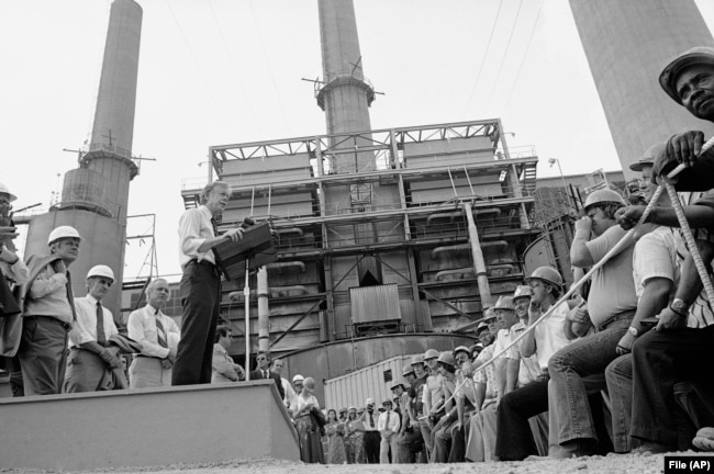 FILE - President Jimmy Carter talks to power plant workers against a backｄrop of tall stacks at the Louisville Gas and Electric Company plant in Louisville, Ky., July 31, 1979.