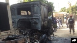 In this photo taken with an iPad policemen stand guard at a burned out truck following an attack by Boko Haram Islamists near an air force base in Maiduguri, Nigeria, Dec, 2. 2013.