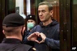 Russian opposition leader Alexey Navalny shows a heart symbol while standing in a defendants' cage during a hearing in the Moscow City Court in Moscow on Feb. 2, 2021.(Moscow City Court via AP)