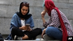 FILE - A woman checks her cell phone sitting with a companion on the steps outside a shopping mall in northern Tehran, Iran, July 2, 2019.
