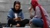 FILE - A woman checks her phone sitting with a companion on the steps outside a shopping mall in northern Tehran, Iran, July 2, 2019.