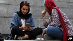 FILE - A woman checks her phone sitting with a companion on the steps outside a shopping mall in northern Tehran, Iran, July 2, 2019.