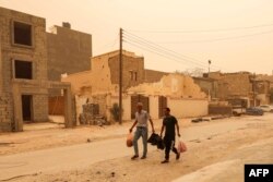 FILE—Two men walk with bags of produce along a street during a sandstorm in Libya's eastern city of Benghazi on April 22, 2024.