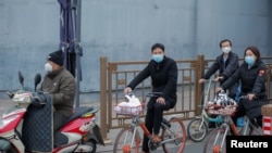 FILE - People on bicycles and electric scooters wear masks as they wait at a traffic light after a yellow alert was issued for smog in Beijing, China, Nov. 14, 2018.