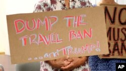 FILE - Critics of President Donald Trump's travel ban hold signs during a news conference with Hawaii Attorney General Douglas Chin, June 30, 2017 in Honolulu. 