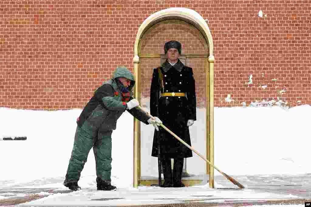 A municipal worker clears snow as an honor guard soldier stands in his station at the Tomb of Unknown Soldier in Moscow, Russia.