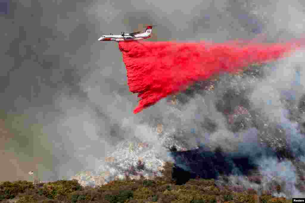 A plane makes a drop as smoke billows from the Palisades Fire at the Mandeville Canyon, in Los Angeles, California, Jan. 11, 2025. 