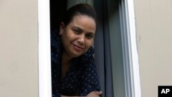 In this Wednesday, May 20, 2020, photo, Wendy De Los Santos, originally from Dominican Republic, stands for a photograph in a window of her home, in Malden, Mass. The 38-year-old Massachusetts resident passed her test to become a U.S. citizen in mid-March. (AP Photo/Steven Senne)