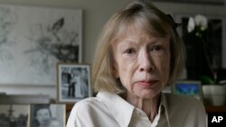 FILE - Author Joan Didion sits in front of a photo of herself holding her daughter, Quintana Roo, and another picture of her daughter's wedding, in her New York apartment Sept. 26, 2005. 