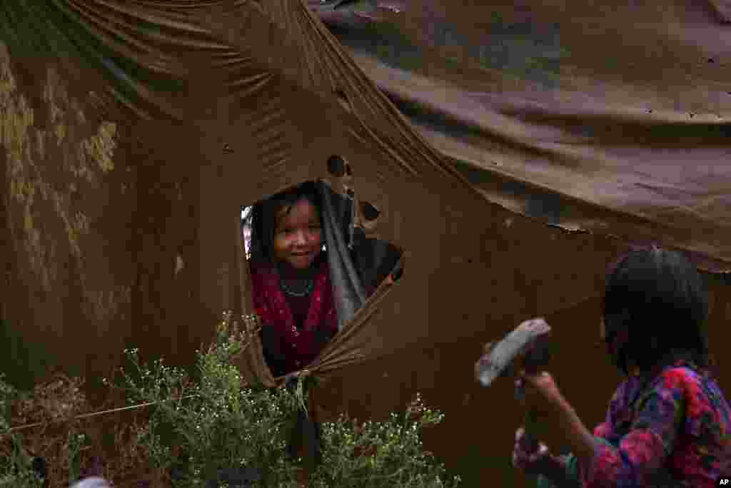 A nomadic girl talks to her sister from a ripped tent during rainfall at a slum in Peshawar, Pakistan.