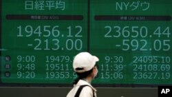 A woman wearing a mask against the spread of the new coronavirus walks past an electronic stock board showing Japan's Nikkei 225 and New York Dow index at a securities firm in Tokyo, April 21, 2020. 