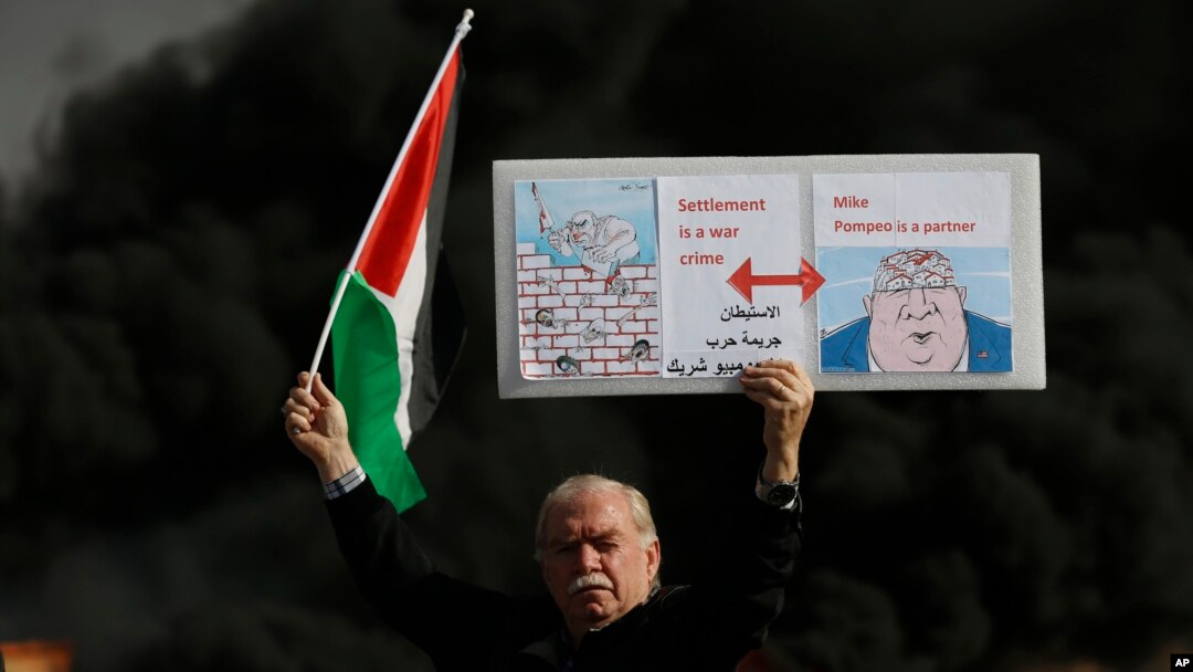 Falastinlik namoyishchi AQSh Davlat kotibi Mayk Pompeo “harbiy jinoyatlarga sherik” deb yozilgan plakat bilan, Ramalloh shahri, 2019-yil, 26-noyabr. 