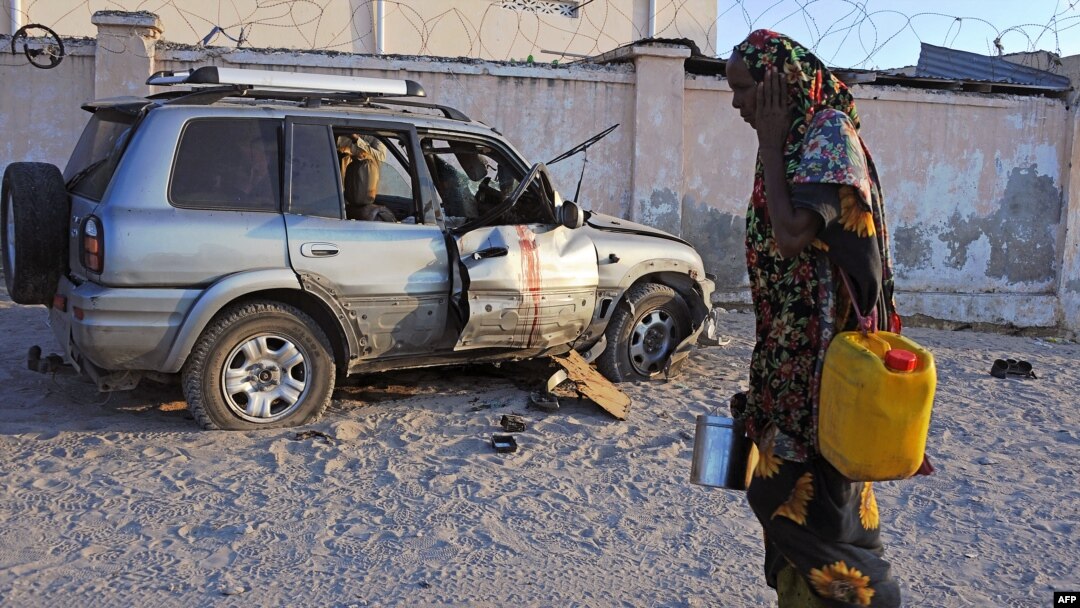 Sorang perempuan Somalia melewati mobil yang terkena serangan bom di Mogadishu (27/11). (AFP/Mohamed Abdiwahab)