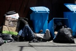 FILE - A homeless man sleeps in front of recycling bins and garbage on a street corner in San Francisco, Aug. 21, 2019.