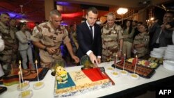 Le président français Emmanuel Macron coupe un gâteau couvert des couleurs du drapeau français lors d’un dîner de Noël avec quelque 700 soldats français de la force anti-djihadiste française sur la base aérienne française de la force Barkhane à Niamey, Niger.