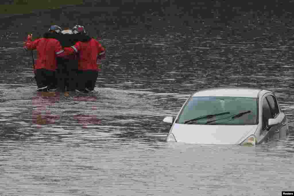 Firefighters rescue a man from his car, after he became trapped in flood water on the A555 near Bramhall, Britain.