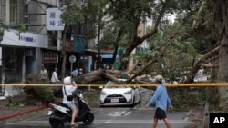 Orang-orang berjalan melintas di area yang porak-poranda akibat Badai Kong-rey di Taipei, Taiwan, Jumat, 1 November 2024. (Foto: Chiang Ying-ying/AP Photo)