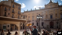 FILE - A waiter with face mask carries beers for customers sitting at a terrace bar in Tarragona, Spain, May 11, 2020. 