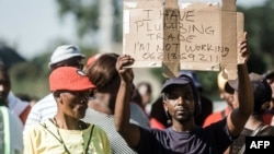 FILE - An unemployed man holds up a sign at the Sugar Ray Xulu stadium in Clermont township, north of Durban, May 1, 2019. (Photo by RAJESH JANTILAL / AFP)