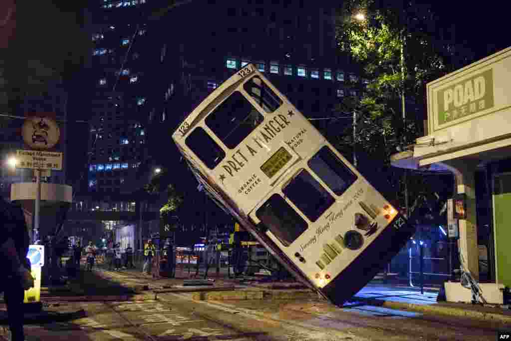 Emergency service personnel and journalists (back) watch as a double-decker tram is lifted by crane after it tipped over on a main road in Hong Kong.