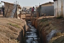 FILE - A boy walks across a wooden bridge over a drainage ditch at the Protection of Civilians (POC) site in Wau, South Sudan, Feb. 1, 2020.