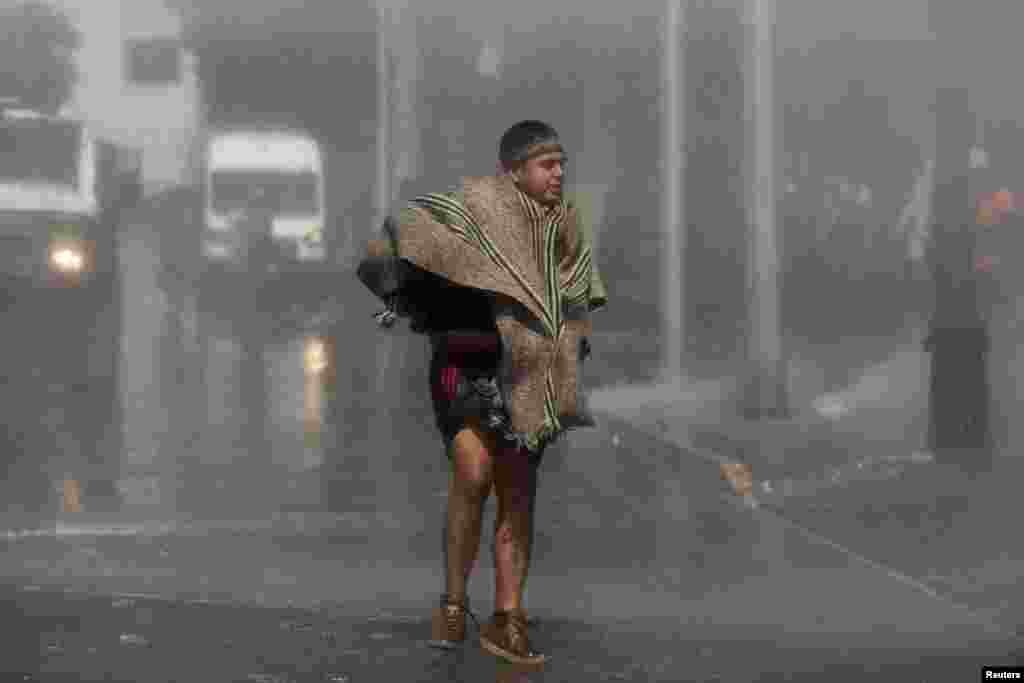 Seorang pria warga suku asli berjalan saat demonstran bentrok dengan polisi anti huru hara selama protes oleh suku asli Mapuche dan aktivis terhadap Hari Columbus di ibu kota Santiago, Cile. (Reuters)&nbsp;