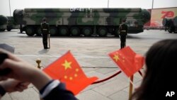 FILE - Onlookers wave Chinese flags as military vehicles carrying DF-41 ballistic missiles roll during a parade in Beijing, China, Oct. 1, 2019.