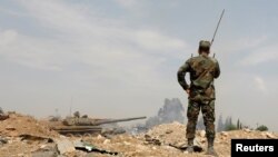 FILE - A Syrian soldier, with a tank in the background, is seen in the al-Qadam area near the Yarmouk Palestinian refugee camp in Damascus, Syria, April 29, 2018.