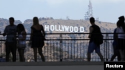 Tourists walk past the Hollywood sign as they visit a shopping complex along Hollywood Boulevard in Hollywood, California, Aug. 3, 2017. 