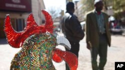FILE - Pedestrians pass a wire and beaded rooster on display outside the Market Theater, background, in Johannesburg's Newtown cultural district, July 30, 2009. 